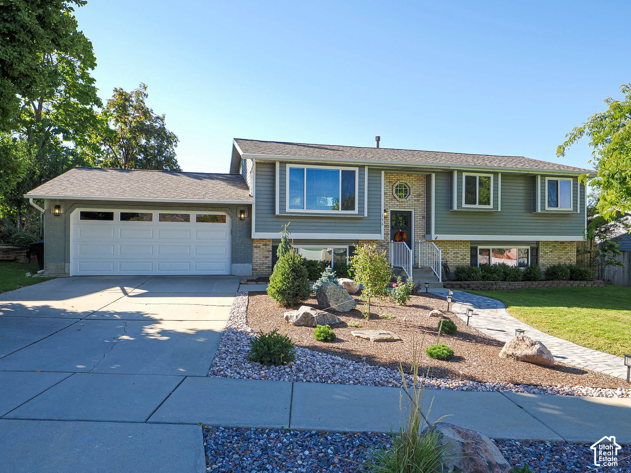 Split-level residence featuring a two-car garage with transom windows, a stone and siding facade, and a paver walkway