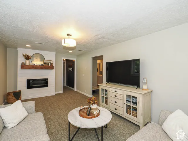 Recessed lighting, electric fireplace with shiplap surround, wood mantel, and carpet flooring
