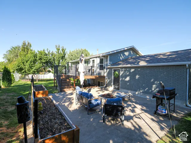 Expansive concrete patio with a raised wood deck, leading to a fenced backyard featuring a grassy lawn and raised planter beds