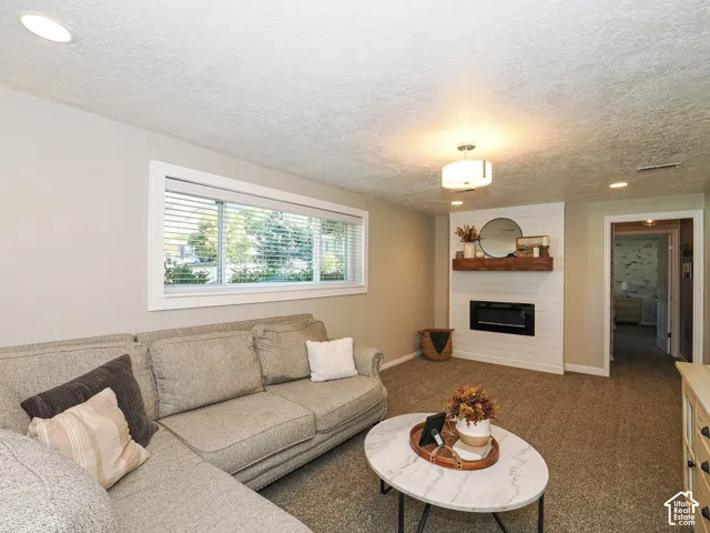Recessed lighting, large horizontal window, shiplap-accented fireplace surround, wood-finish mantel, and carpet flooring