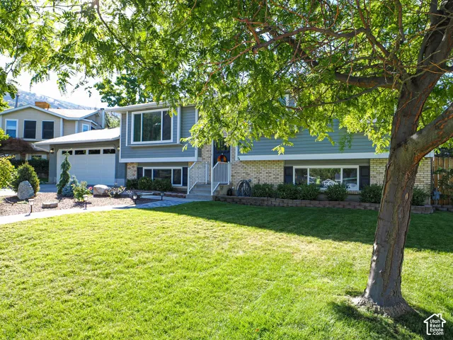 Split-level residence featuring a two-car garage, light brick and horizontal siding exterior, and a manicured front lawn