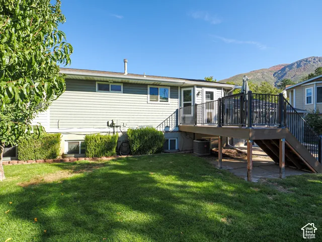 Expansive backyard featuring a multi-level deck with dark railing, mature landscaping, and a mountain backdrop