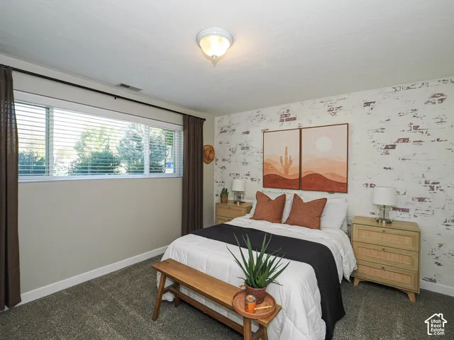 Wall-to-wall carpeting, window with blinds, overhead flush-mount lighting, and an accent wall with a distressed brick-style finish