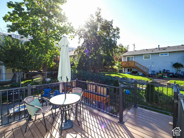 Expansive deck with composite decking and dark railings, overlooking a tiered backyard with mature trees, established landscaping, and a chain link fence