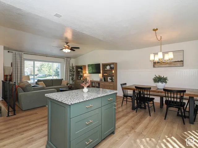 Expansive open-concept living space featuring wood-finish flooring, a vaulted ceiling, and a central island with a stone countertop