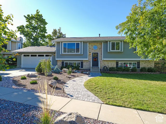 Split-level residence featuring a two-car garage, stone and siding exterior, and a paver walkway
