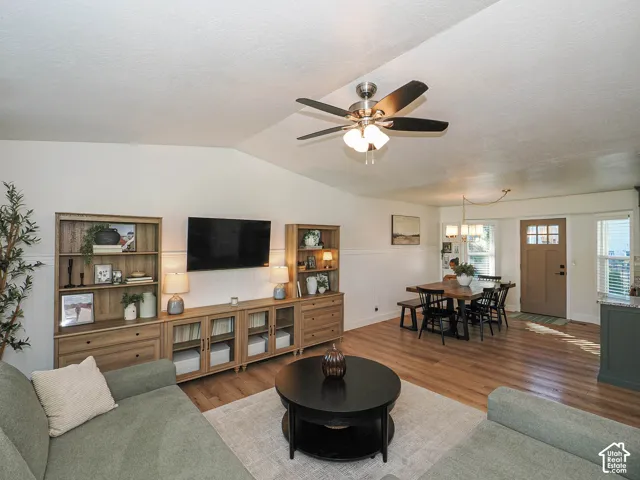 Vaulted ceiling with ceiling fan, wood-finish flooring, wainscoting, and a wood-panel entry door