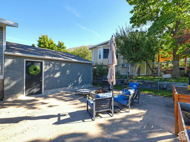 Concrete patio surface, brick exterior structure, built-in raised garden beds, mature trees, and chain-link fencing