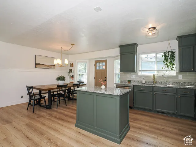 Kitchen and dining area featuring wood-finish flooring, a kitchen island with a stone countertop, dark green cabinetry, and a subway tile backsplash