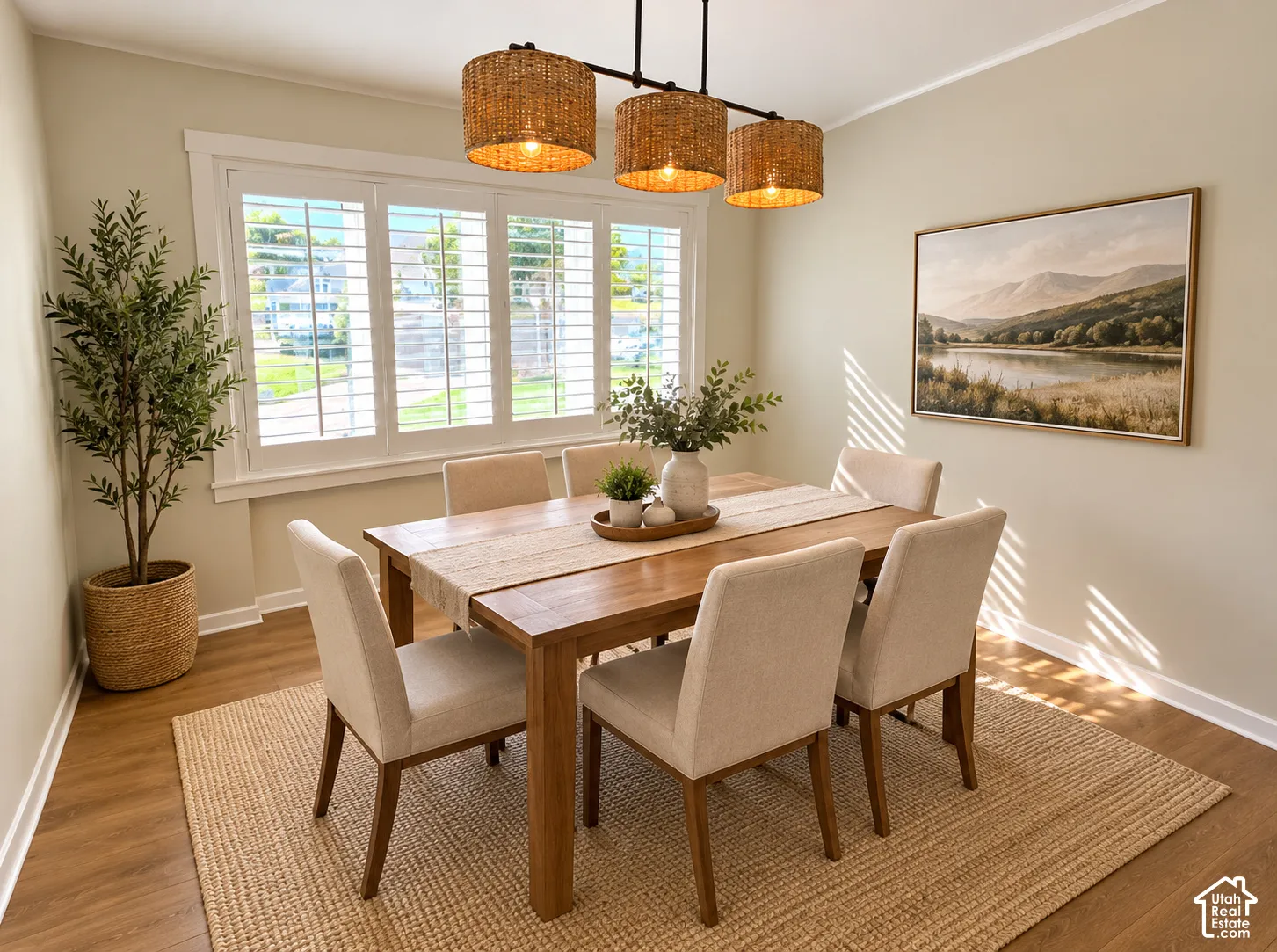 Three-light linear chandelier with woven shades, plantation shutters, and wood-finish flooring