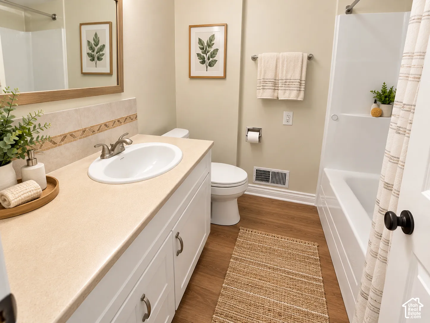 Bathroom featuring a white vanity with a neutral countertop and integrated sink, framed wall mirror, wood-finish flooring, and a shower-tub combination with a wall-mounted fixture