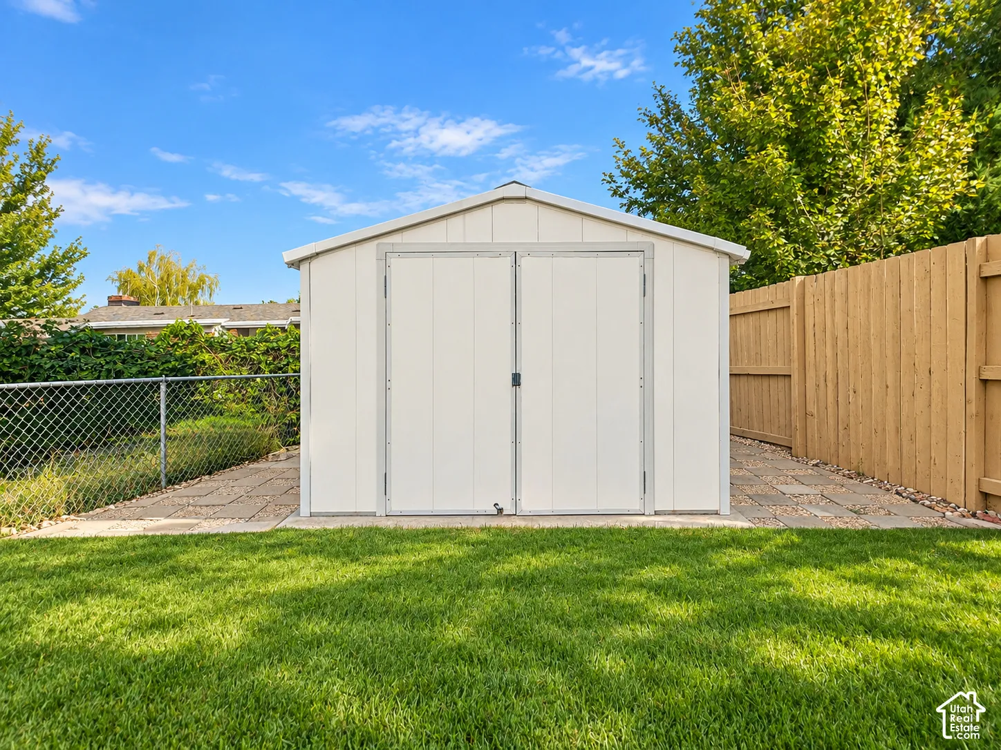 Detached storage shed with double doors, wood fencing, and a chain link fence