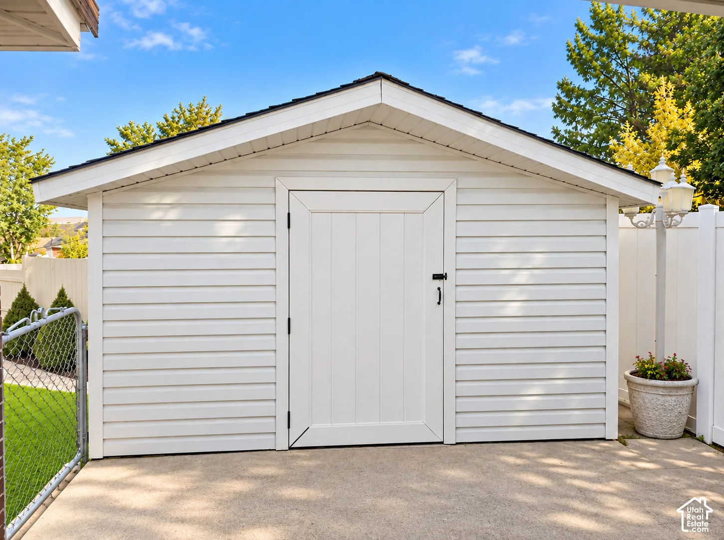 Detached storage shed with white horizontal siding and a dark shingle roof