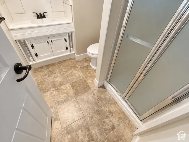 Basement bathroom, Tiled flooring, white vanity with integrated sink, dark bronze hardware, frosted glass shower enclosure, and white toilet