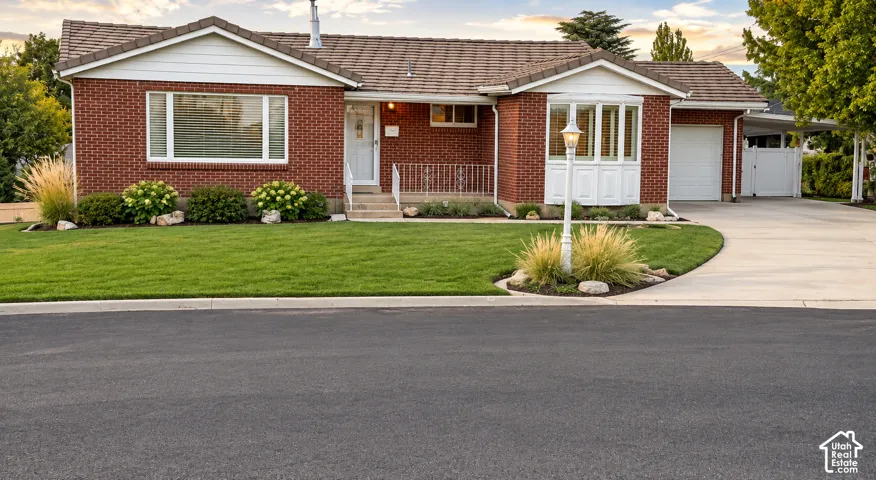Brick exterior with white trim, bay window, manicured lawn, and paved driveway leading to an attached garage