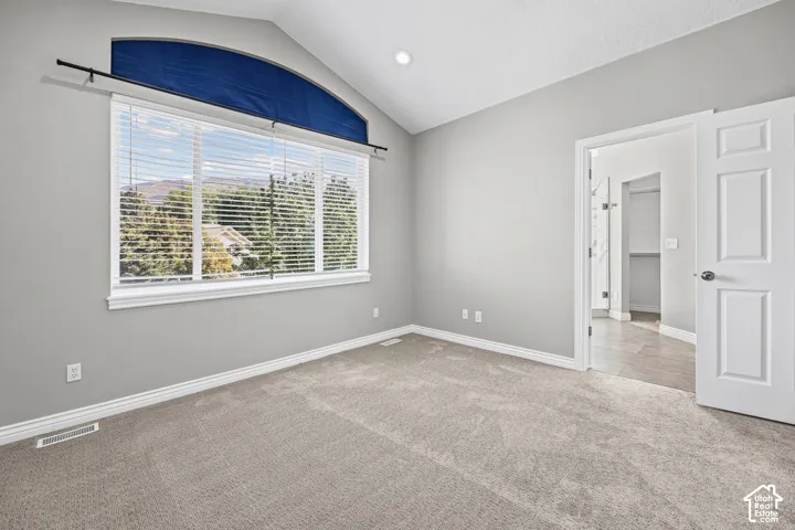 Vaulted ceiling, arched transom window, large window with blinds, neutral carpet flooring, and a white paneled door