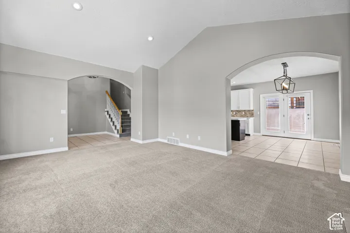 Vaulted ceiling with recessed lighting, arched doorways, carpet flooring, tile flooring, and a modern geometric light fixture