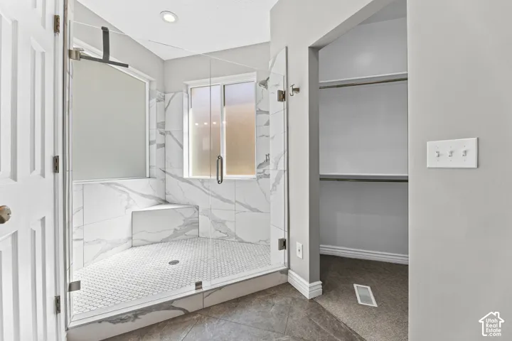 Walk-in shower with clear glass enclosure, white marble-look tile walls, integrated shower bench, and white hexagonal floor tiles