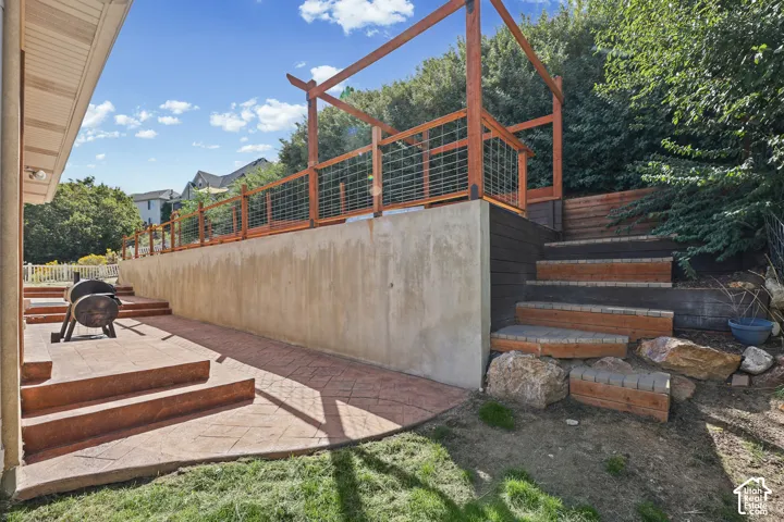 Stamped concrete patio with integrated steps, terraced landscaping with wood-finish retaining walls, and a wood railing with grid infill