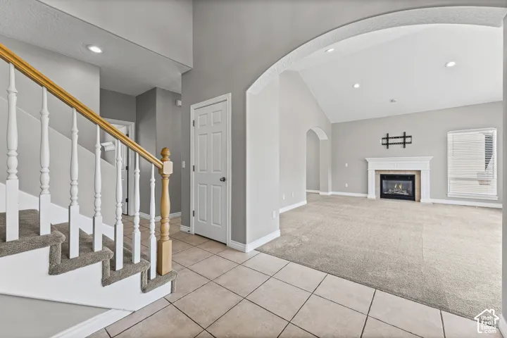 Tile flooring, carpeted stairs with wood railing, vaulted ceiling, arched doorway, and a fireplace with mantle