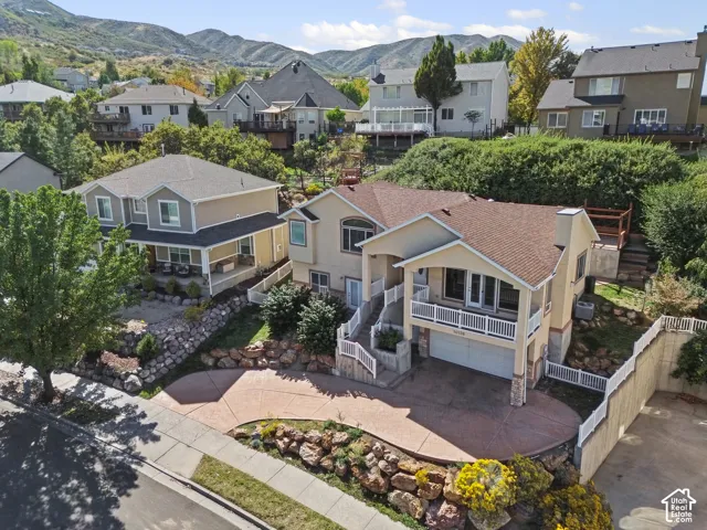 Stamped concrete driveway, terraced landscaping with natural rock elements, second-level balcony, mountain backdrop, and covered porch
