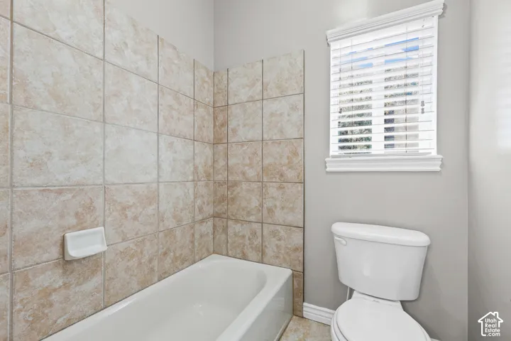 White porcelain bathtub with a ceramic tile surround and a toilet
