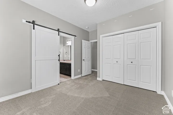 Neutral gray wall paint, light-colored carpeting, white barn door, white bi-fold closet doors, and recessed ceiling lighting
