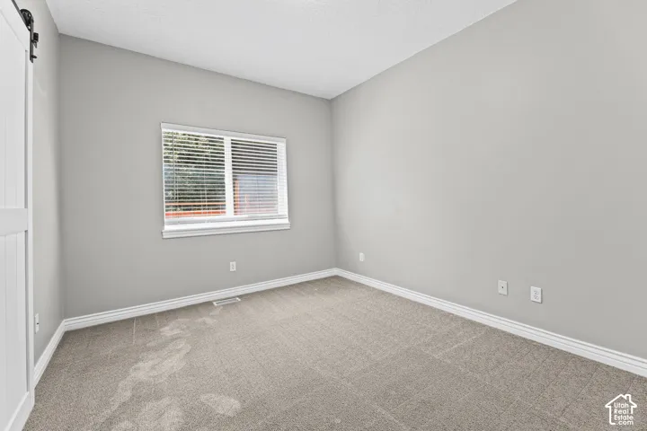 Neutral wall color, window with horizontal blinds, textured carpet flooring, white trim, and a white barn door