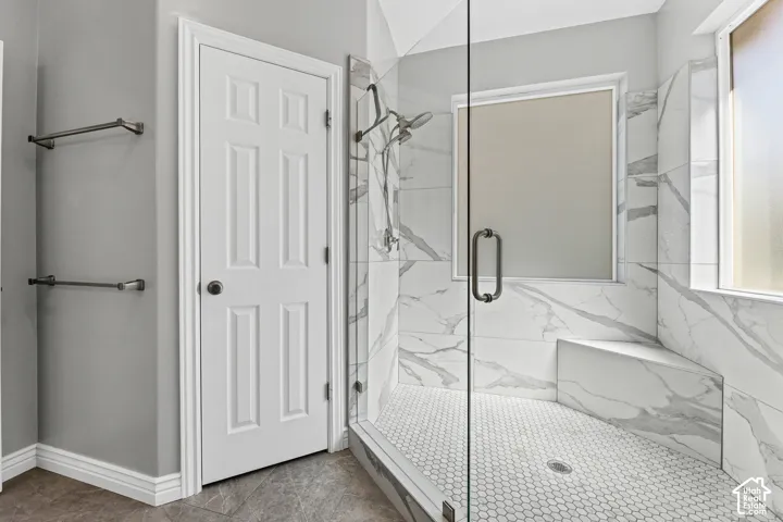 Glass-enclosed shower with white hexagon tile flooring, white marble-look tile walls, and a built-in shower bench