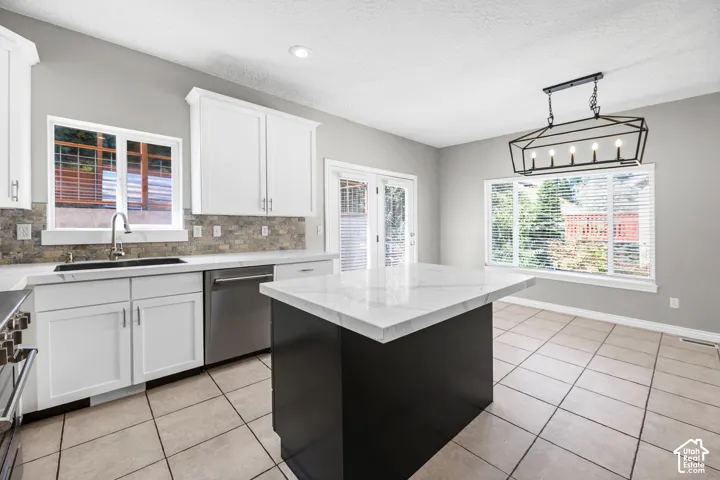 White shaker cabinetry, stone-look tile backsplash, stainless steel appliances, large center island with a stone countertop, and a modern geometric chandelier
