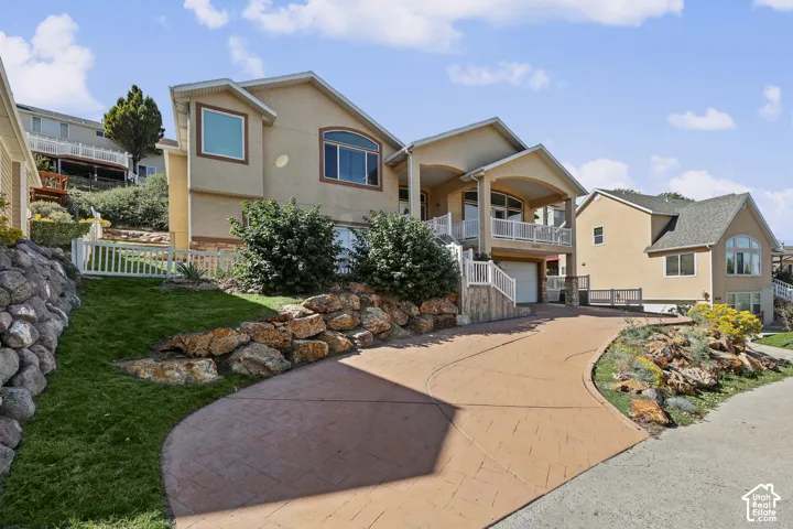Stucco exterior with multiple balconies, stamped concrete driveway, and tiered landscaping with rock retaining walls