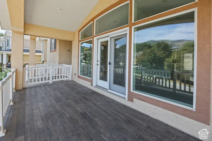 Covered outdoor deck with wood-finish plank flooring, white railing, and sliding glass door