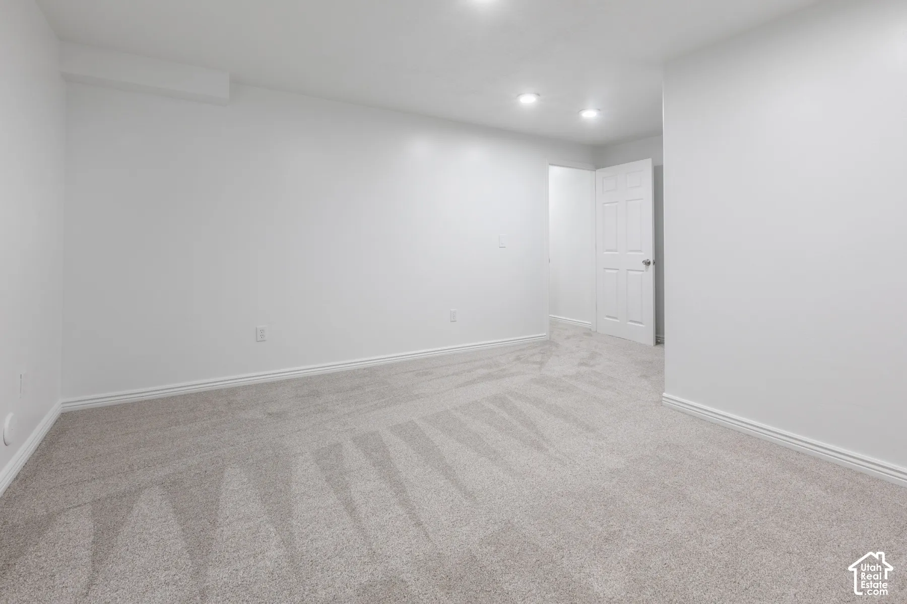 Recessed lighting illuminates neutral carpeting and white walls