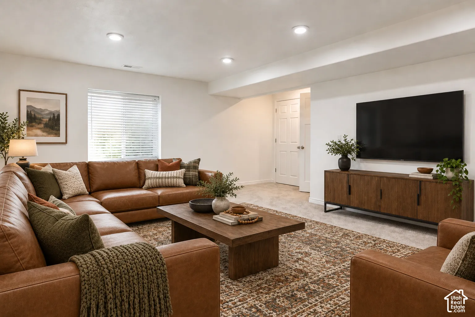 Recessed ceiling lighting illuminates a spacious room featuring a window with blinds, wood-finish flooring, and a paneled door