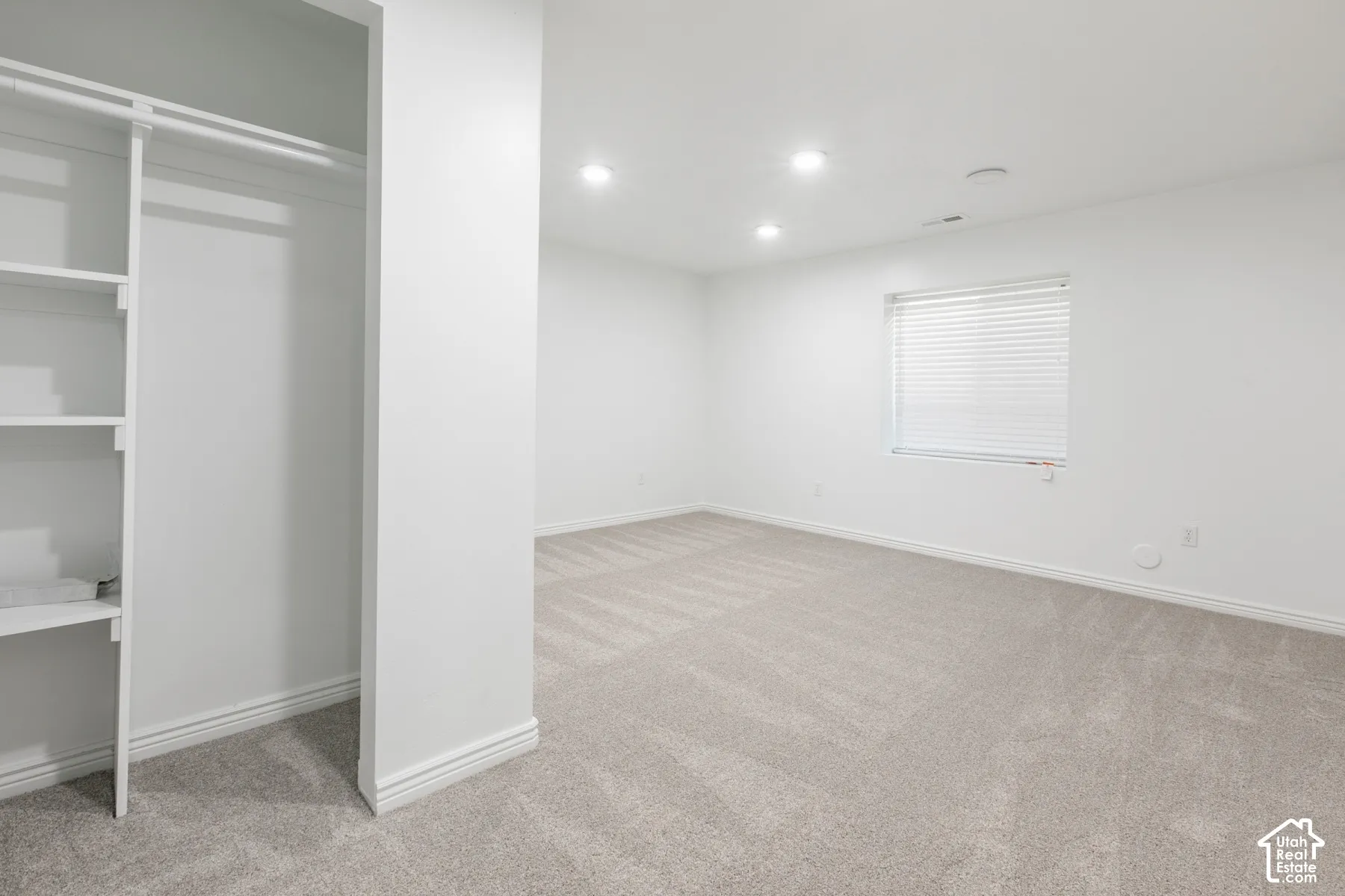 Built-in closet shelving, recessed lighting, window with blinds, and light-colored carpeting