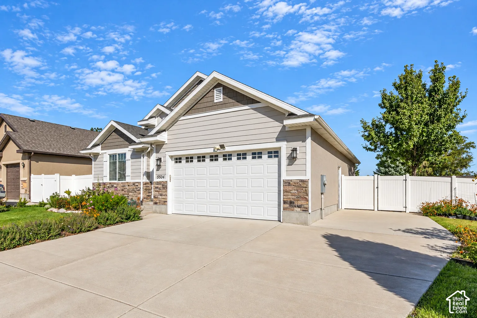 Property exterior featuring siding and stone veneer accents, an attached garage, a paved driveway, and a white privacy fence with a gate