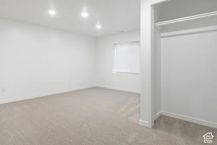 Recessed lighting illuminates a neutral carpeted room with a built-in closet and window with horizontal blinds