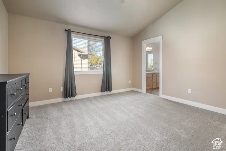 Vaulted ceiling with neutral wall tones, window with horizontal blinds, gray carpeting, and a doorway opening to a bathroom with dual vanity