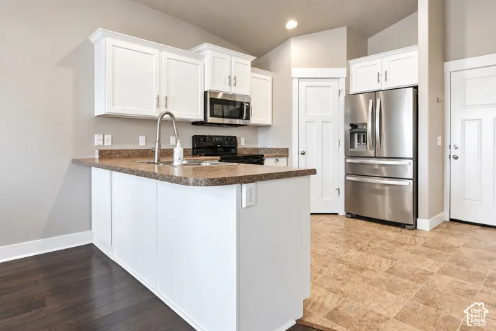 White cabinetry, stainless steel appliances, breakfast bar, brown countertop, and dark wood-finish flooring
