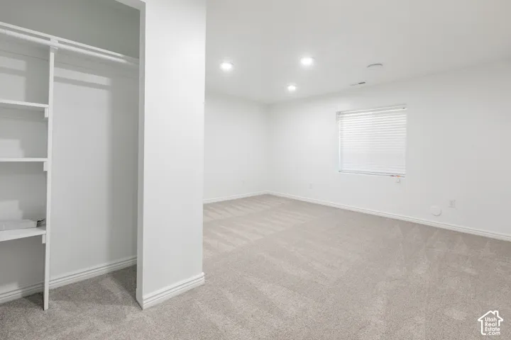 Built-in closet shelving, recessed lighting, window with blinds, and light-colored carpeting