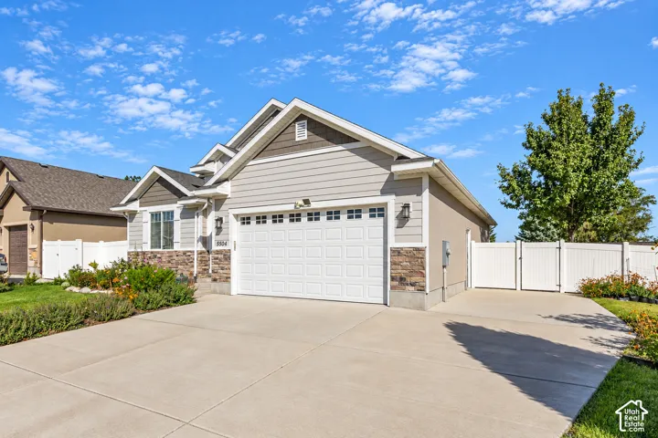 Property exterior featuring siding and stone veneer accents, an attached garage, a paved driveway, and a white privacy fence with a gate