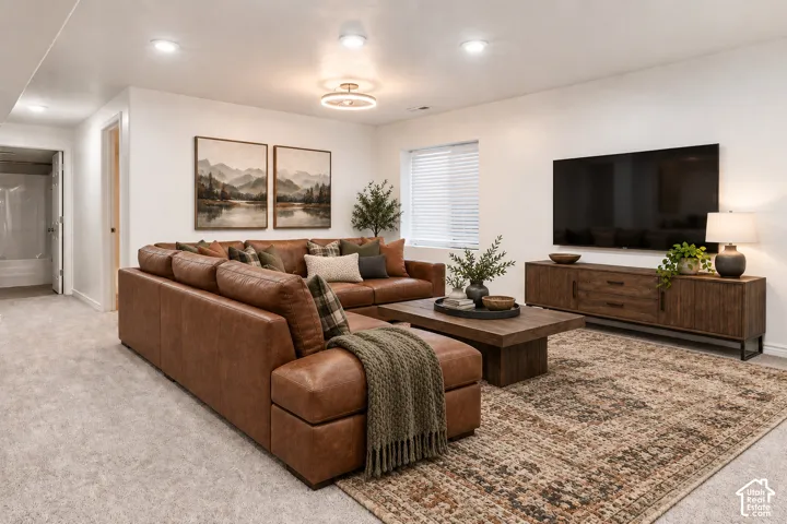 Recessed lighting and a modern semi-flush mount fixture illuminate this space, featuring light-colored carpeting and a window with blinds