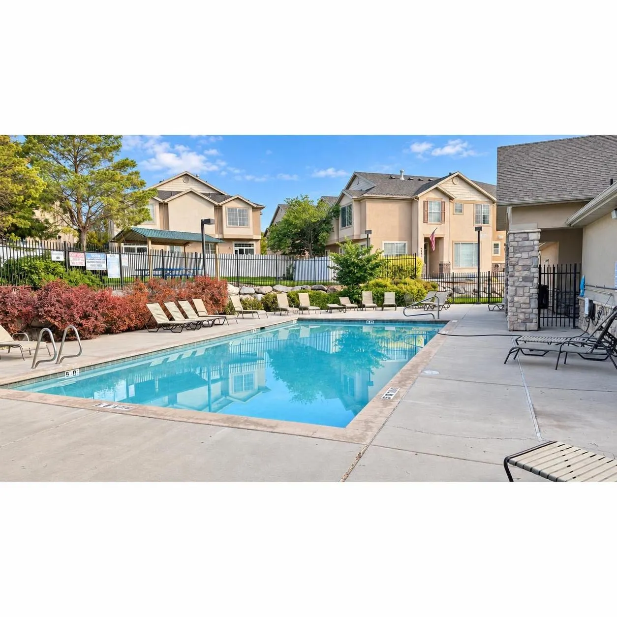 Community swimming pool with a concrete deck, surrounding landscaping, and a shaded outdoor seating area