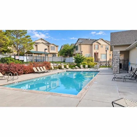 Community swimming pool with a concrete deck, surrounding landscaping, and a shaded outdoor seating area