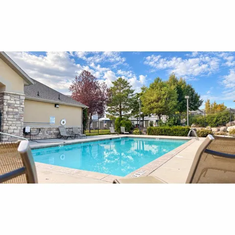Rectangular swimming pool with concrete decking, surrounded by a stone and stucco building facade, mature trees, and fencing