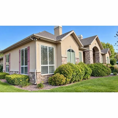 Stucco exterior with stone accents, multiple large windows, a pitched roof, and mature landscaping