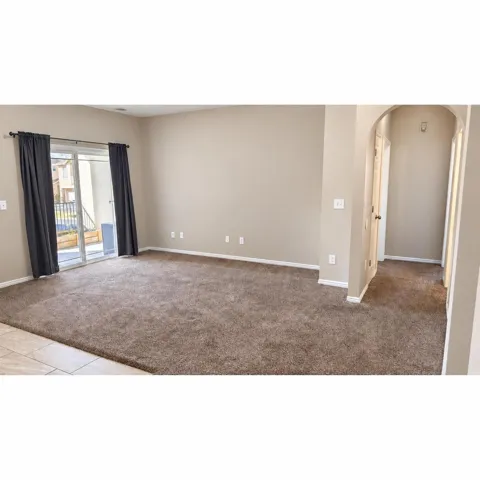 Spacious room featuring neutral carpeting, light-toned walls, and a sliding glass door leading to an exterior balcony