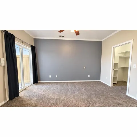 Primary Bedroom with a ceiling fan, crown molding, a sliding glass door, and an open walk-in closet with built-in shelving