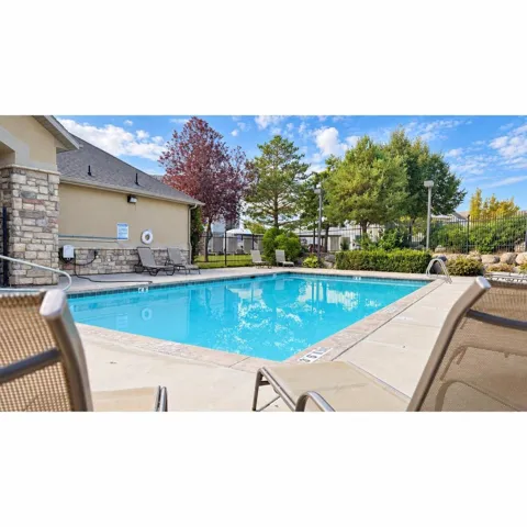 Fenced swimming pool with a concrete surround, featuring a stone and stucco building