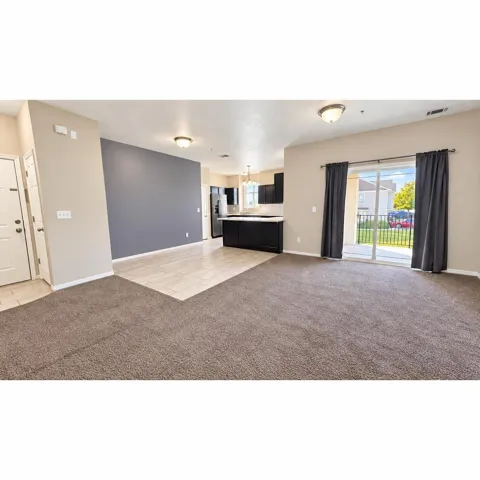 Open-concept living area with carpet and tile flooring, a kitchen featuring dark cabinetry and light countertops, and a sliding glass door opening to an exterior patio